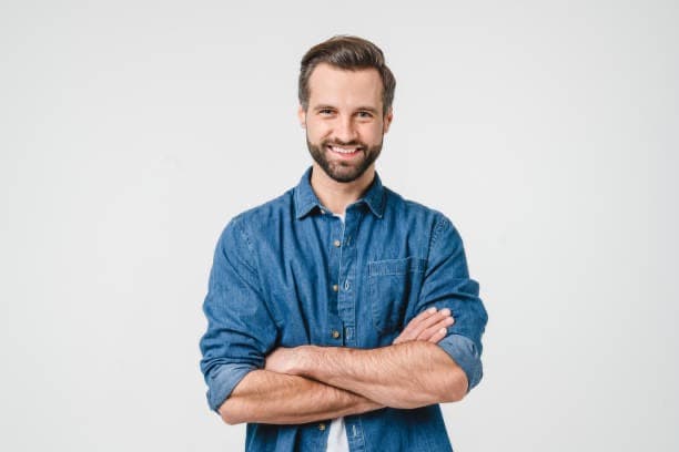 Lächelnder Mann mit Bart im blauen Jeanshemd und verschränkten Armen vor weißem Hintergrund.